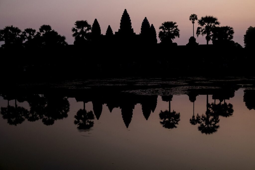 Angkor Wat silhouetted against a pink dawn sky and reflected in the moat