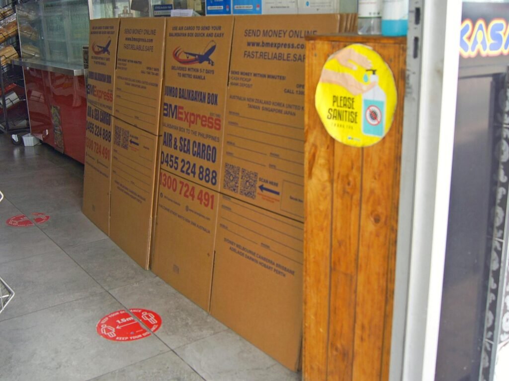 Stack of flat-packed jumbo balikbayan boxes advertising air and sea cargo to the Philippines, leaning against a counter in a Filipino shop